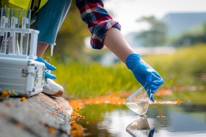 A young researcher collects a water sample from a pond