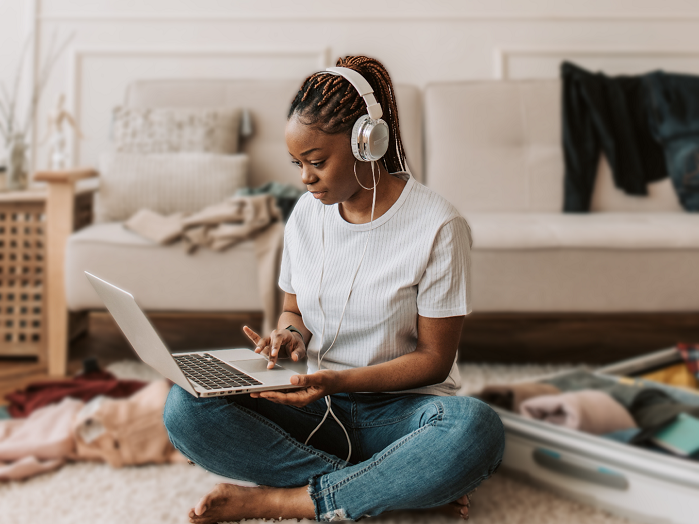 Student in her bedroom sitting on the floor on her laptop listening to music