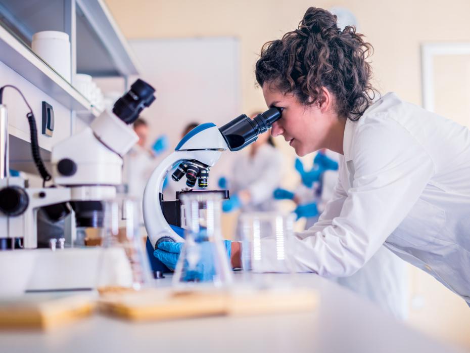 An early career researcher looking through a microscope in a lab