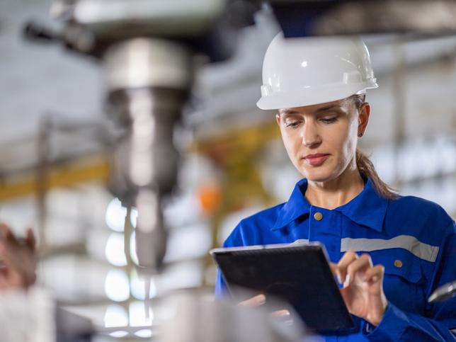 An engineer controls the quality using a tablet device to inspect the drilling machine in the factory