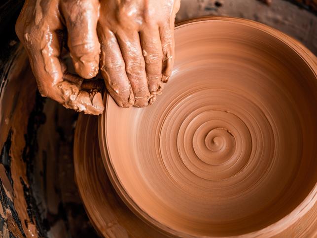 Hands work on a clay pot
