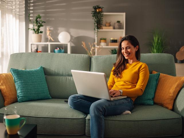 A woman sits on a sofa with a laptop