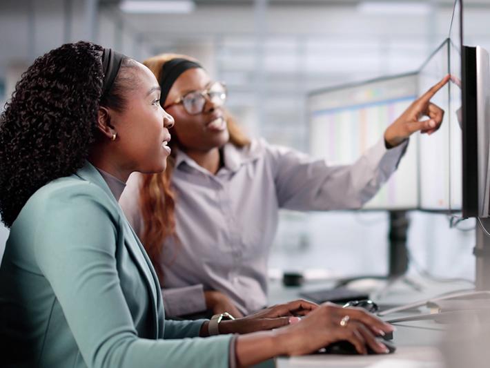 Young black woman looking at screen with help from older black woman, job shadow concept