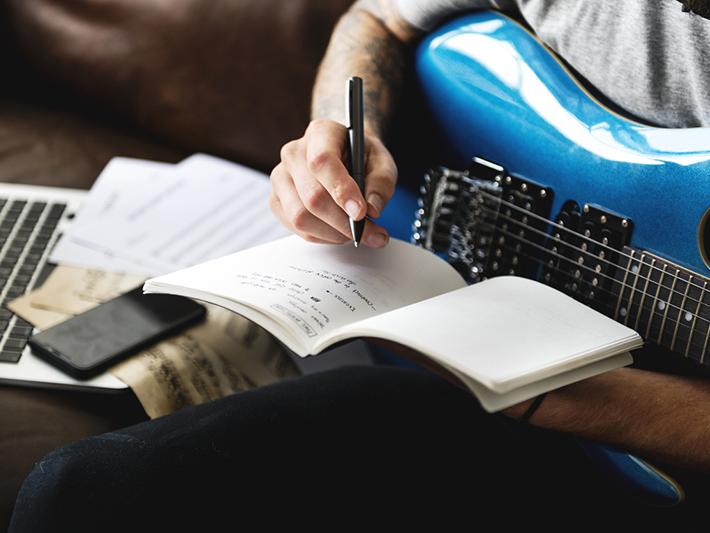 Detail of man writing music on an electric guitar