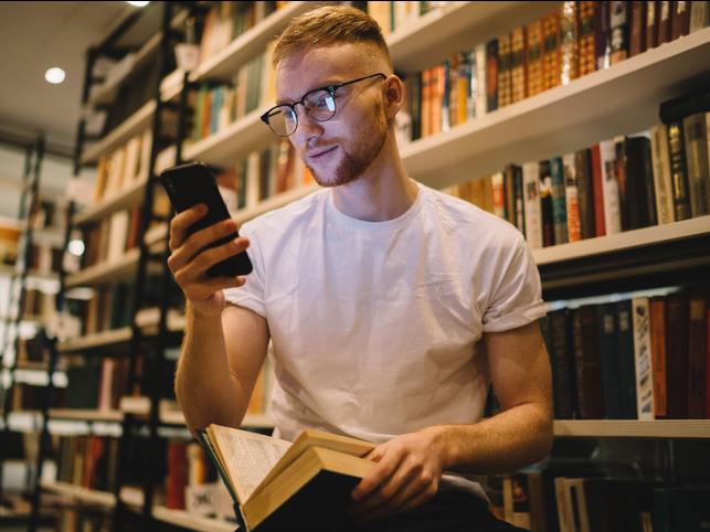 A student looks up from a book to check his smartphone 