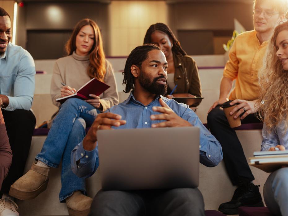 A university lecturer explaining a concept while sitting amongst students 
