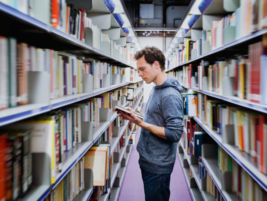 A man reads a book between the aisles of a university library