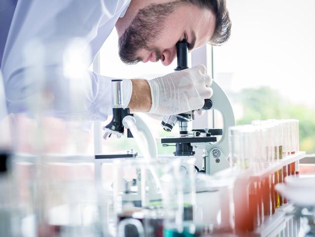 A close-up of a lab worker looking through a microscope