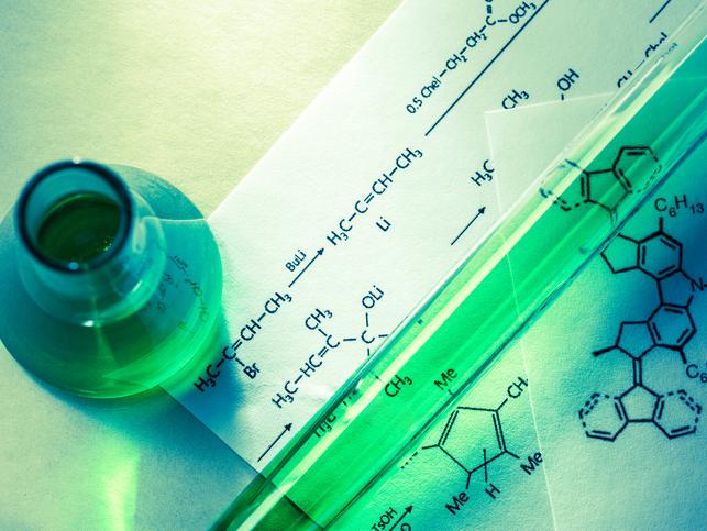A vial of green liquid sits on a sheet of reaction formulas