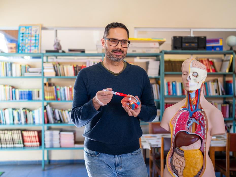 A biology teacher standing next to a demo human body with its organs exposed