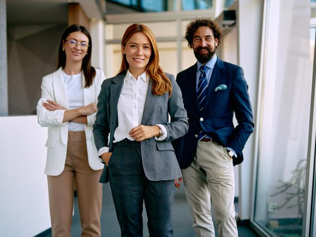 Three business professionals standing in an office and smiling to camera