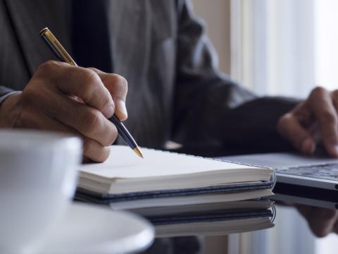 Man working with laptop, pen and paper and coffee, OERs