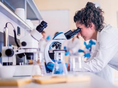 Young female scientist examining a sample through a microscrope