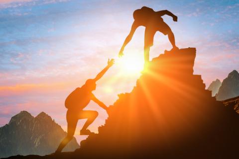 A mountain climber helps another up a steep hill