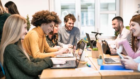 A group of students laugh while using laptops