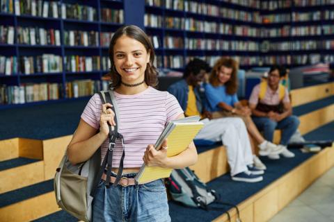 A female student holding a notebook stands in a library