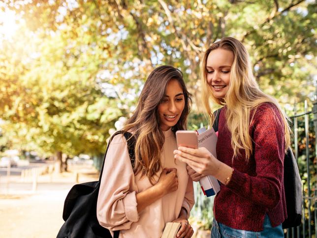 Female students looking at phone outdoors illustrating embodied learning