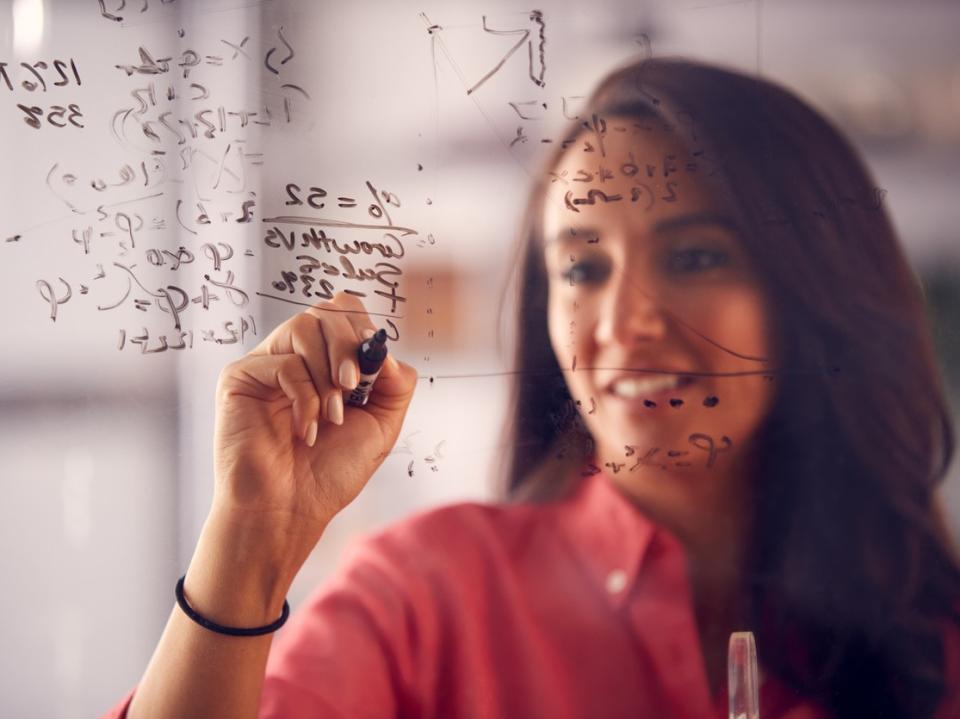 A woman writing out equations on a glass screen