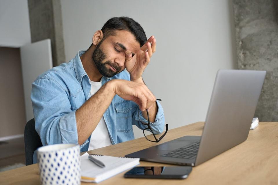 A tired looking man at his laptop rubbing his eyes 