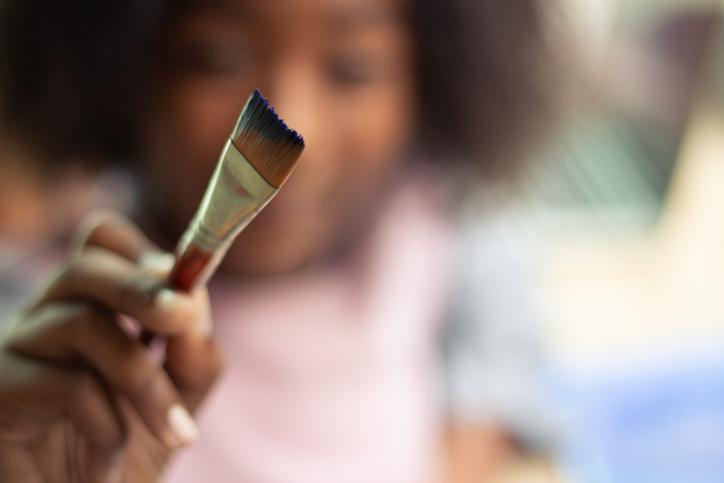 A Black artist holds a paintbrush out to the camera