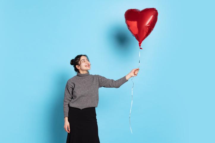 A smiling woman holds a red, heart-shaped helium balloon