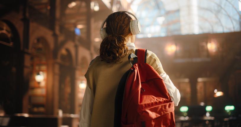 A student walks into a library, wearing headphones