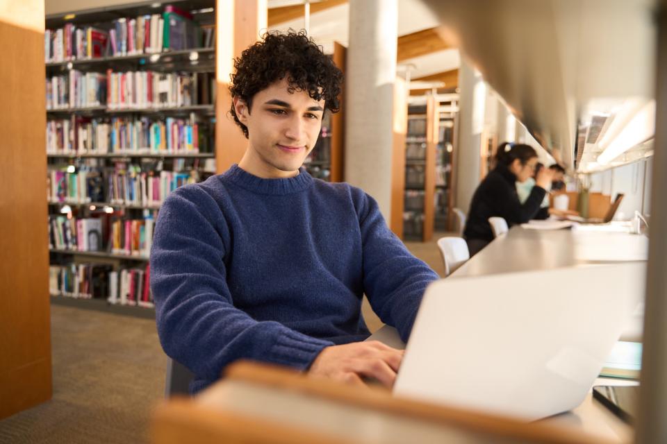 A male student working on his laptop in the library