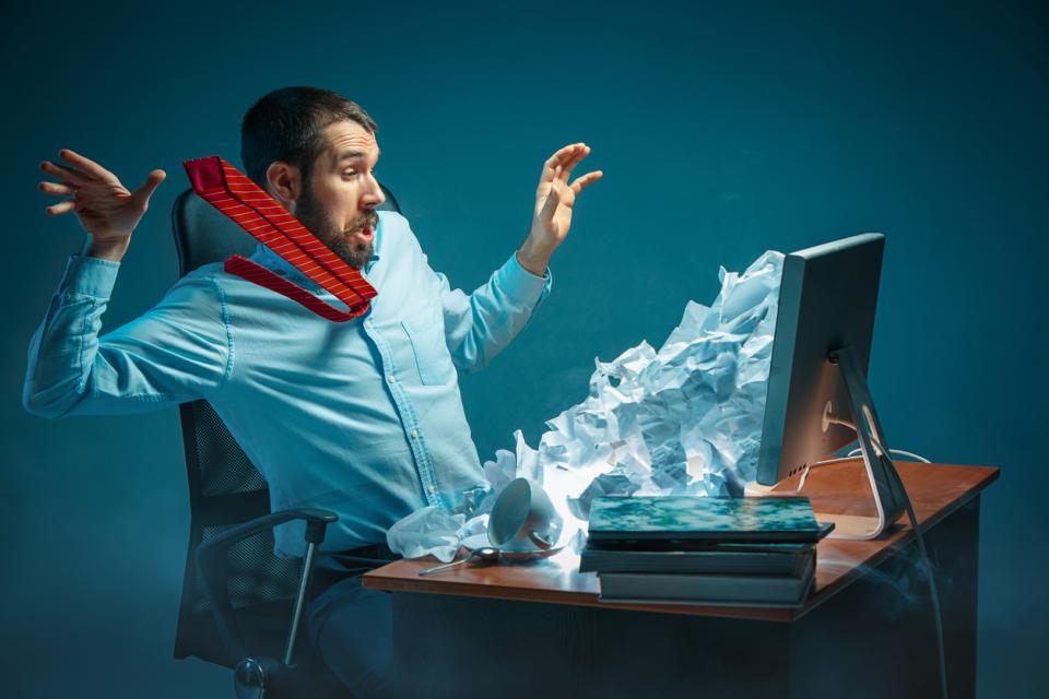 Young man looking stressed as his inbox explodes out of his screen