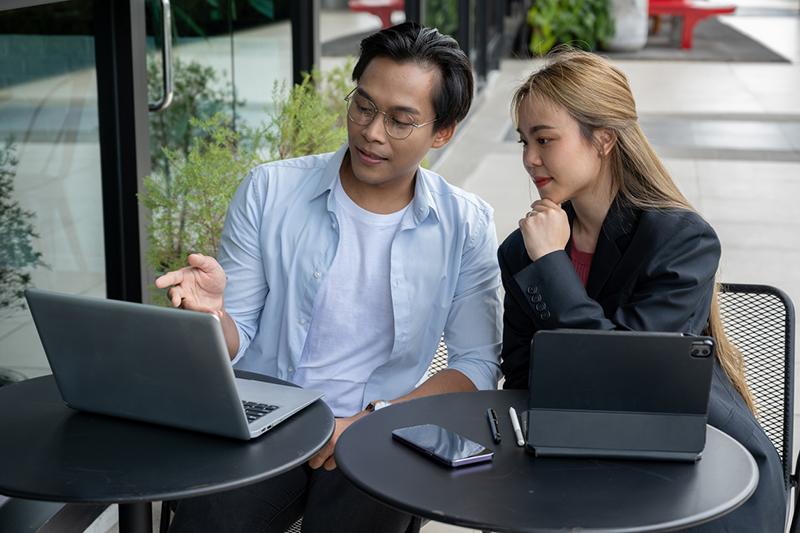Two Asian students in a coffee shop looking at a laptop