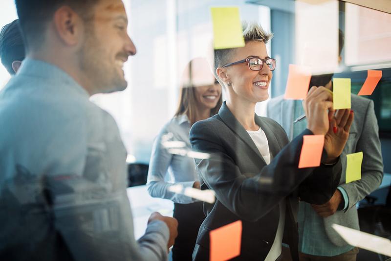 Colleagues looking at sticky notes on glass wall