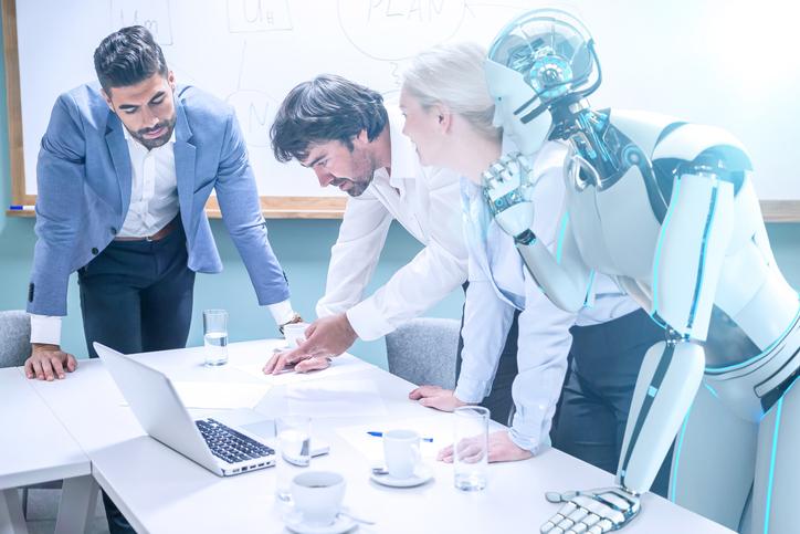 A robot leans over a meeting of humans