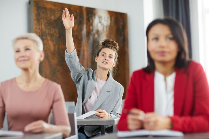 A student raises a hand at the back of class