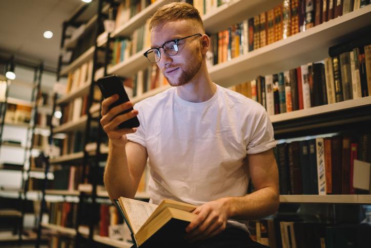 A student looks up from a book to check his smartphone 