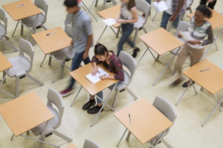 A student sits an exam hall as her peers leave around her