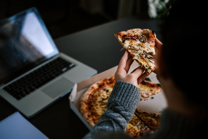 A student eats pizza in front of a laptop