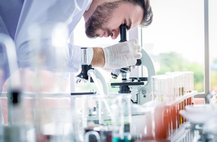 A close-up of a lab worker looking through a microscope