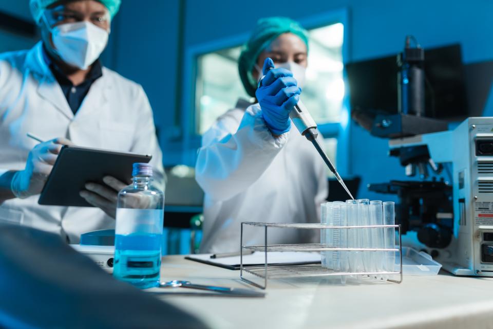 Two masked scientists fillin test tubes in a lab