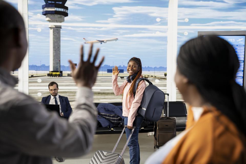 A young woman waves goodbye to family at an airport