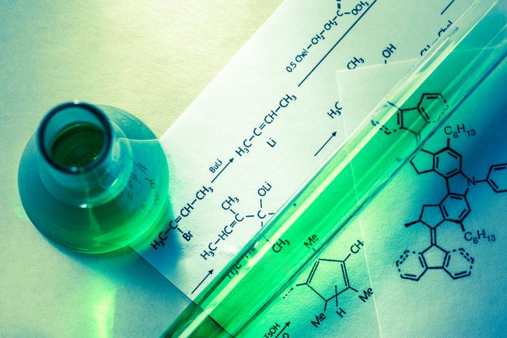 A vial of green liquid sits on a sheet of reaction formulas