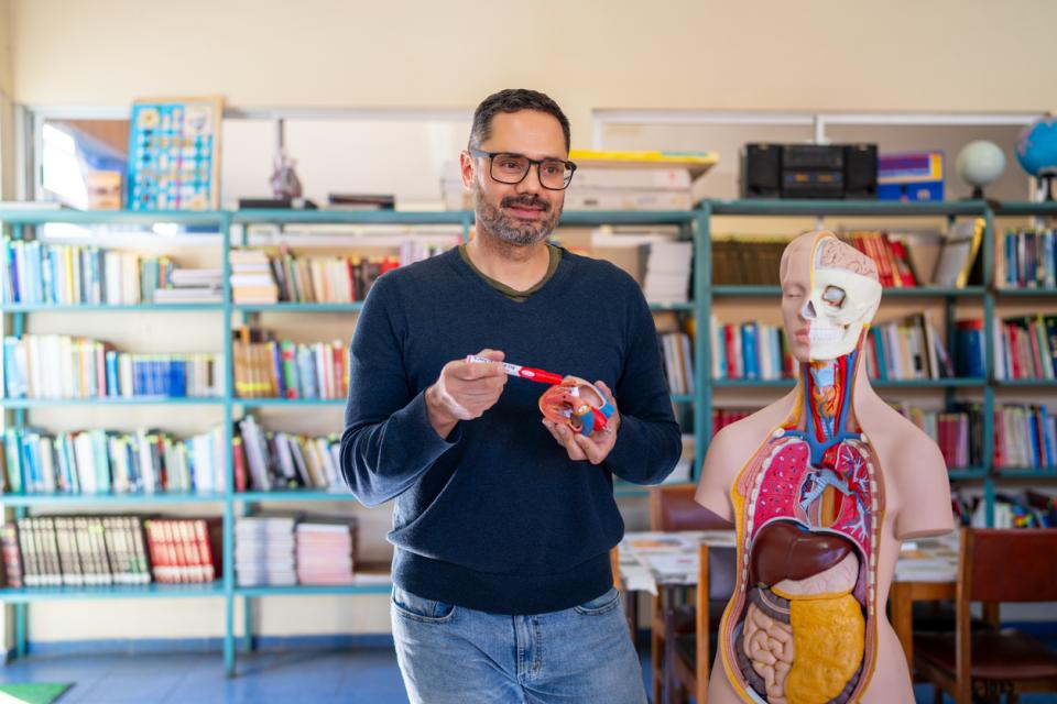 A biology teacher standing next to a demo human body with its organs exposed