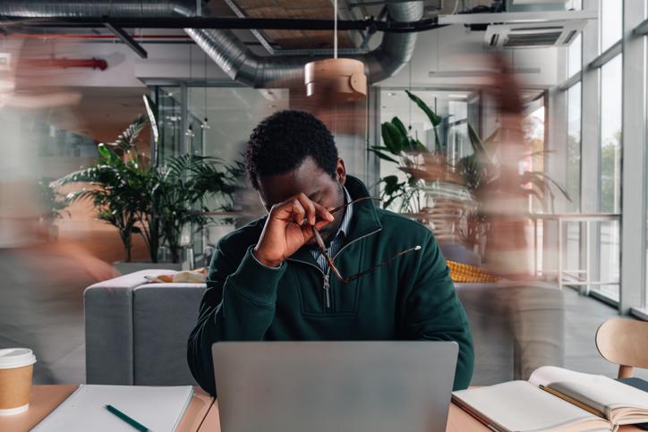 A man at a desk rubs his forehead