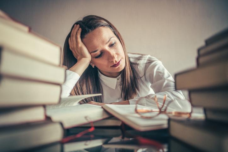 An academic surrounded by books looks stressed