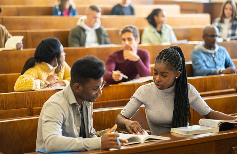 Two students in lecture hall look at a book