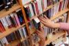 A hand taking a book out of a shelf in a library