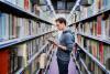 A man reads a book between the aisles of a university library